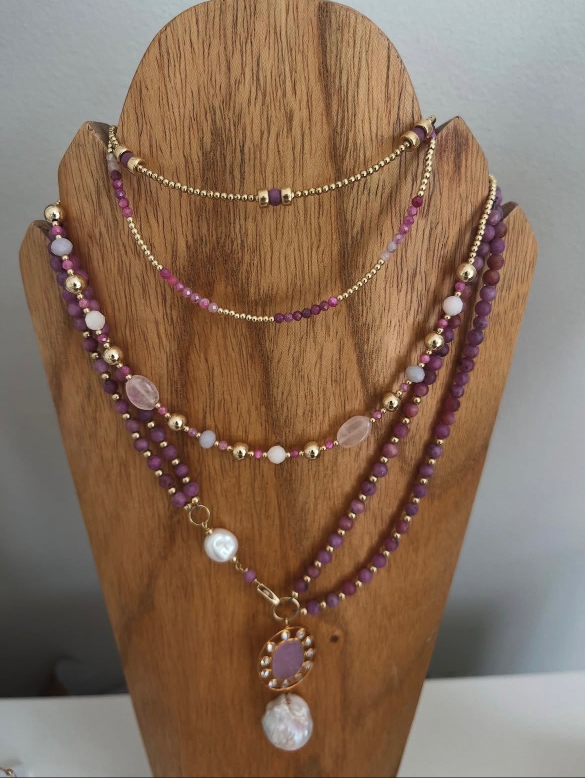 Delicate purple and gold beaded necklace displayed on a wooden stand